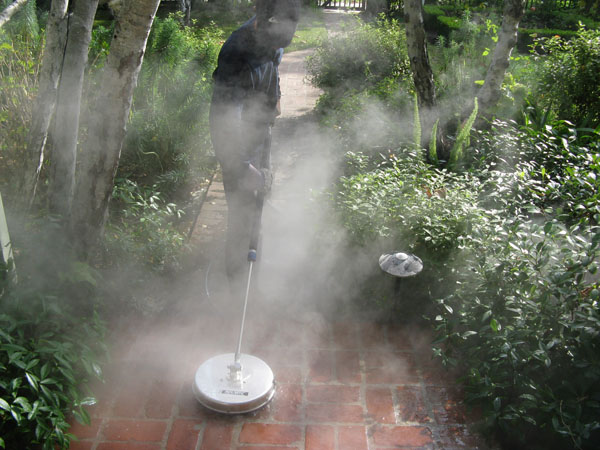 Technician pressure washing a brick walkway with a surface cleaner